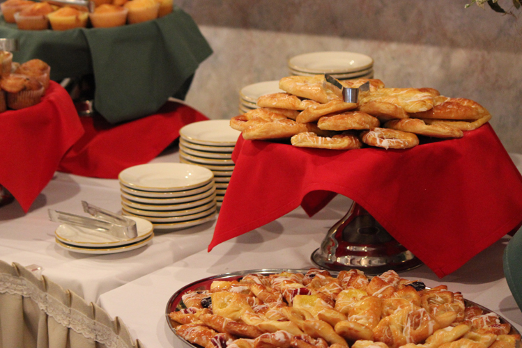 A table adorned with clean stacked dessert dishes and platters of danish and muffins with red and green tablecloths.