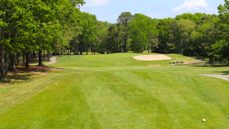 The view from the tee box to the par 3 8th green at Ocean Acres Country Club. The tee box has white, gold, and red tee markers and, there is a right, greenside bunker protecting the green.