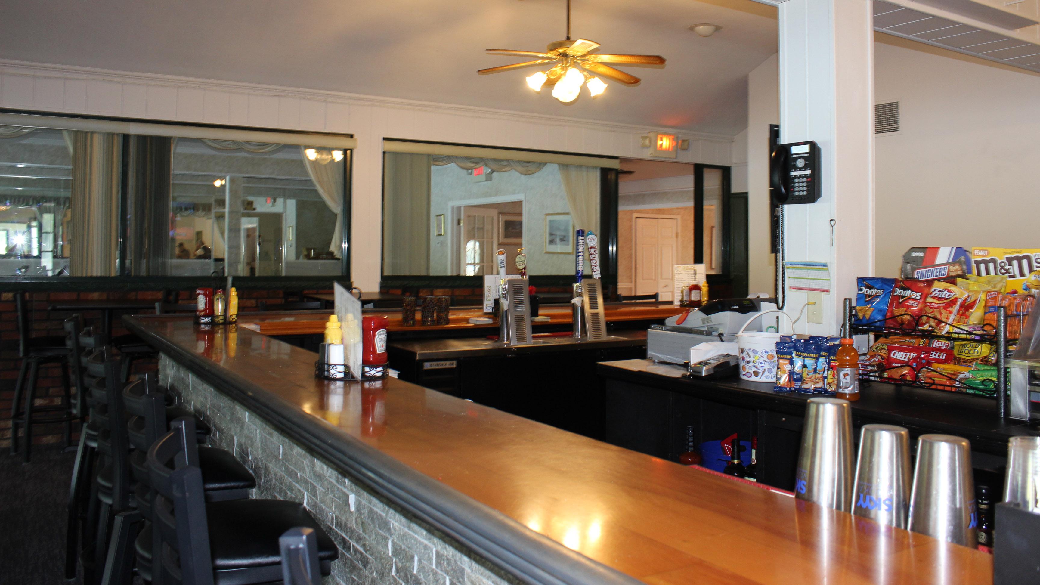 The bar countertop runs across the foreground. Bar stools are set at the counter. Various snacks, beer taps for draught beer, and cups and condiments can be seen in and around the bar.
