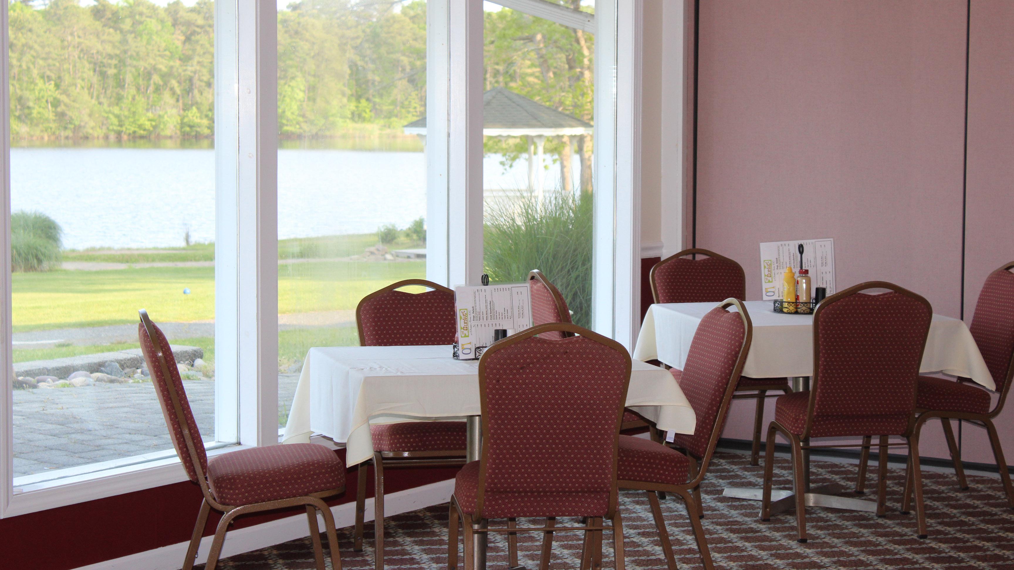 Square tables seating four with table cloths and set with condiments and menus. Holiday Lake, the gazebo, and the 10th tee box can be seen through the windows.